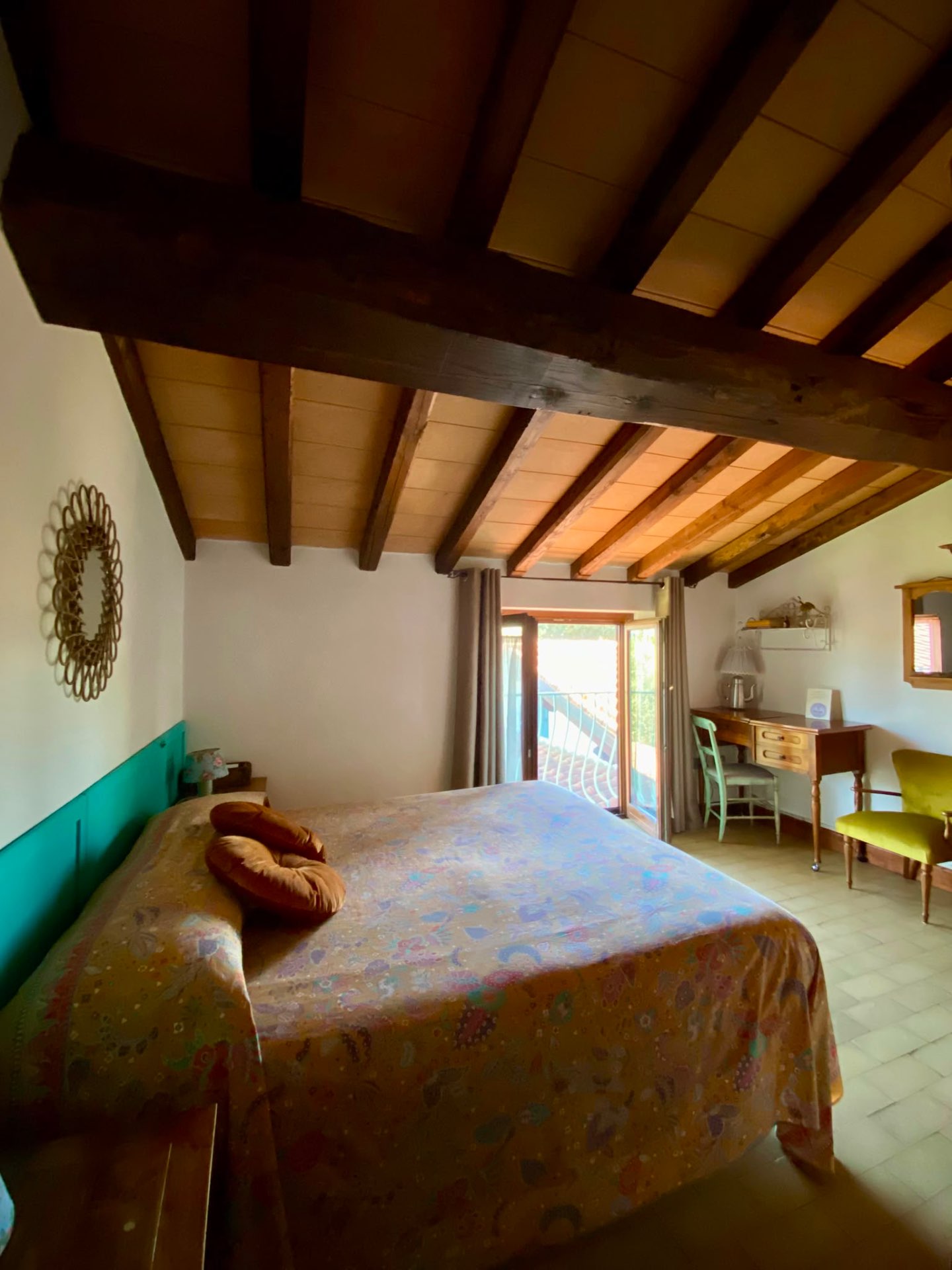 Camera Edera con letto a copriletto fantasia, scrivania in legno e poltrona verde
