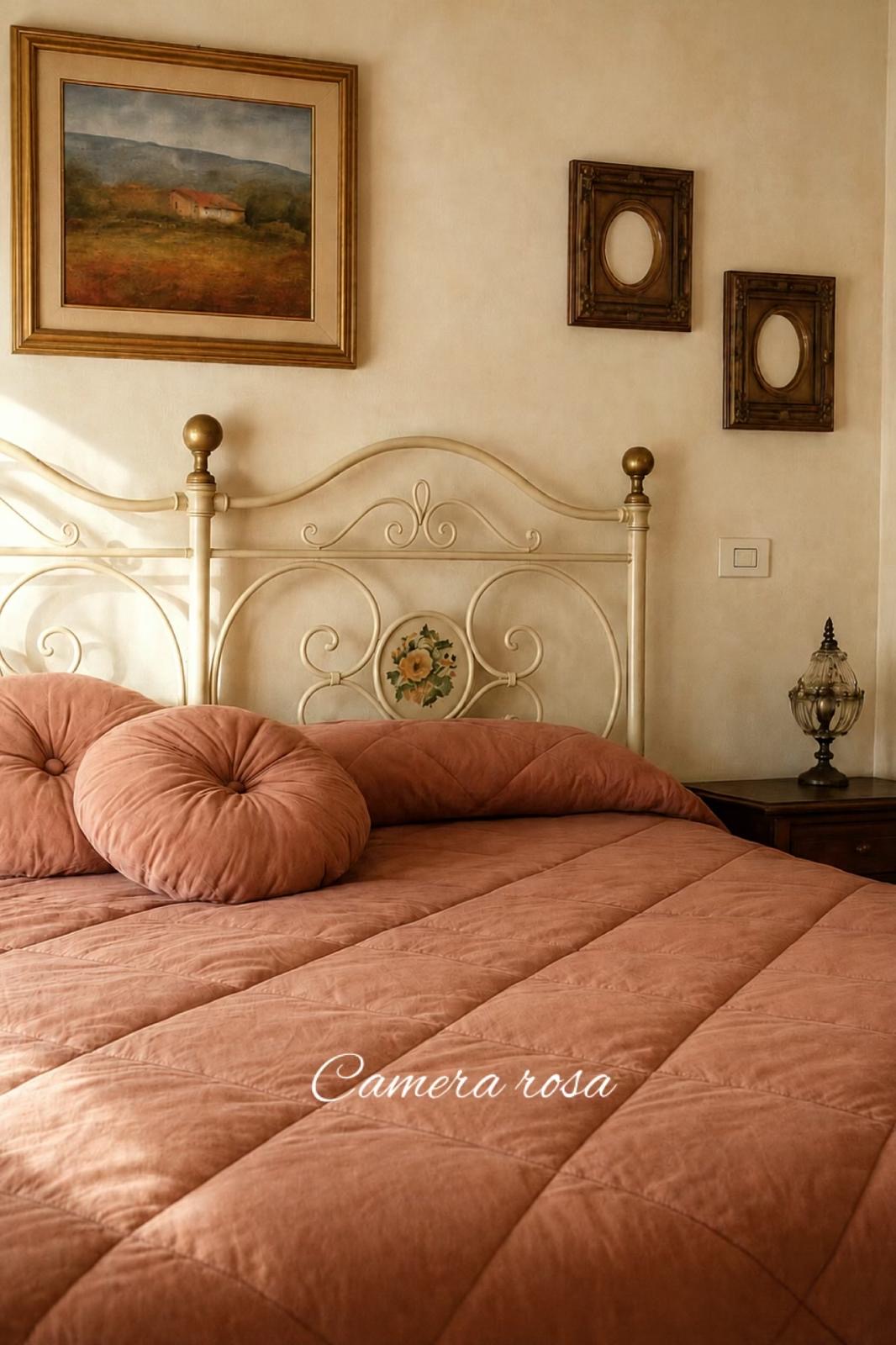 Camera Rosa con copriletto rosa antico e letto in ferro battuto